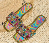 Glitter In Gold Sandals with colorful jewel embellishments on woven mat.